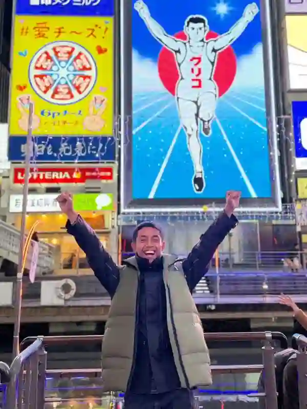 大阪・道頓堀のグリコ看板前で、両手を挙げて喜びを表すインドネシア人若者